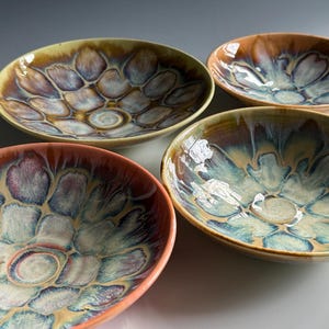 May include: Four ceramic bowls with a floral pattern. The bowls have a glossy finish with a color palette of orange, yellow, blue, and brown. The bowls are round and have a shallow depth.