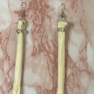 May include: A pair of bone-shaped earrings with silver wire wrapped around the top. The earrings are hanging from silver hooks.