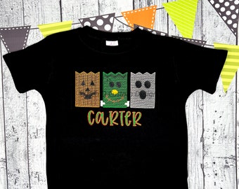 May include: Black t-shirt with an embroidered design of three Halloween-themed characters, a jack-o-lantern, a monster, and a ghost. The name "carter" is embroidered below the characters.