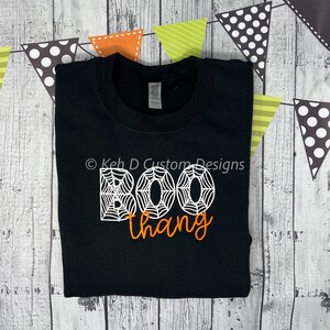 May include: Black sweatshirt with white spiderweb lettering that reads "BOO thang" in orange.
