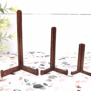 May include: Three wooden picture stands of varying sizes. The stands are made of dark brown wood and have a triangular base.