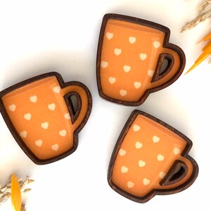 May include: Three wooden mugs with a brown rim and a light orange background with white hearts.