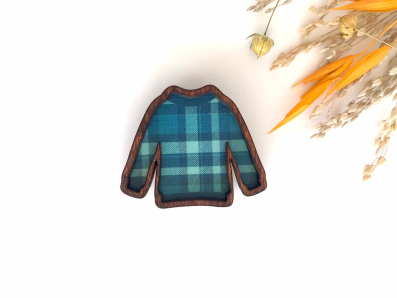 May include: A wooden pin shaped like a sweater with a blue and green plaid pattern.
