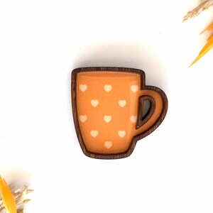 May include: A wooden mug with a brown rim and handle. The mug is painted orange with white hearts.