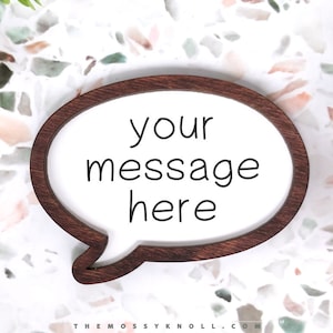 May include: A wooden speech bubble with a white background and the text "your message here" in black. The speech bubble is on a white and brown terrazzo surface.