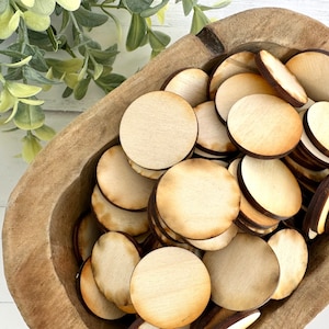 May include: A wooden bowl filled with a large quantity of unfinished, round wooden circles. The circles are various shades of brown and have a natural wood grain.