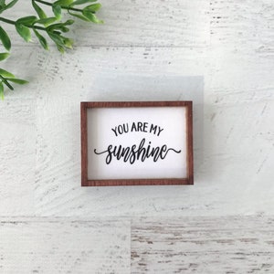 May include: A small wooden sign with a white background and brown frame. The sign says "You are my sunshine" in black cursive lettering.