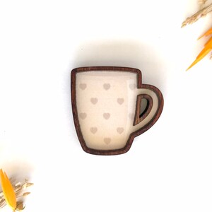 May include: A wooden mug with a brown rim and a white interior with a pattern of small hearts. The mug is a decorative item.