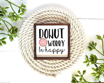 May include: A small wooden sign with a brown frame and a white background. The sign says "Donut Worry Be Happy" with a pink donut graphic.
