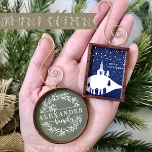 May include: Two Christmas ornaments with gold-colored hooks. One is round with "The Alexander Family" in white script on a green background. The other is rectangular with a church scene and the words "merry christmas".