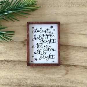 Peut inclure: Petit panneau rectangulaire en bois avec l'inscription "Silent night, holy night. All is calm, all is bright" en &eacute;criture &eacute;l&eacute;gante. Le panneau a un fond blanc avec du texte noir et des &eacute;toiles, encadr&eacute; par une bordure marron fonc&eacute;.