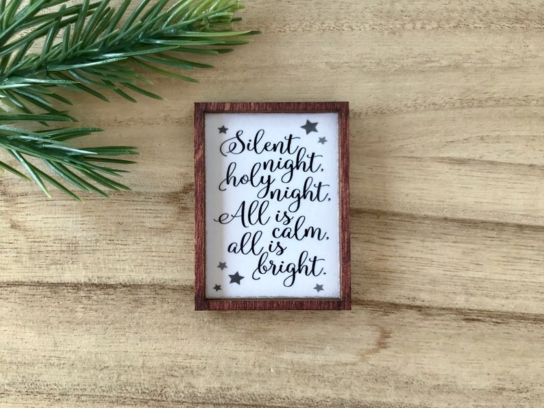 Peut inclure: Petit panneau rectangulaire en bois avec l'inscription "Silent night, holy night. All is calm, all is bright" en &eacute;criture &eacute;l&eacute;gante. Le panneau a un fond blanc avec du texte noir et des &eacute;toiles, encadr&eacute; par une bordure marron fonc&eacute;.