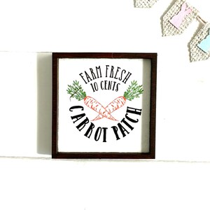 May include: A wooden sign with a brown frame and white background. The sign says "Farm Fresh 10 Cents Carrot Patch" with two crossed carrots in the center.