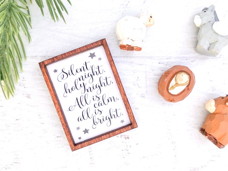 Peut inclure: Un panneau encadr&eacute; en bois avec le texte "Silent night. holy night. All is calm. all is bright." est entour&eacute; de petites figurines d&eacute;coratives d'un mouton, d'un &acirc;ne, de J&eacute;sus b&eacute;b&eacute; et d'une vache. Le panneau et les figurines sont sur une surface blanche.