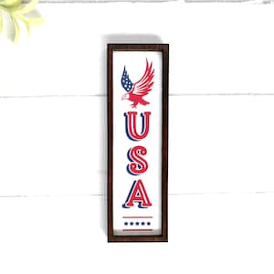 May include: A wooden sign with a red, white, and blue American flag and eagle design. The sign says "USA" in red, white, and blue letters.