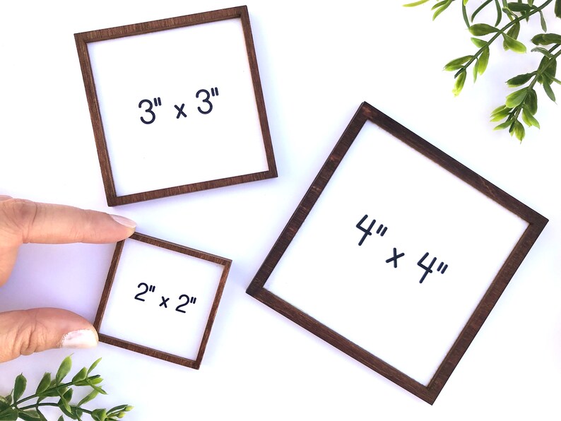 May include: Three square wooden frames with white centers. The frames are different sizes: 2" x 2", 3" x 3", and 4" x 4". Each frame has dark brown wooden borders. The text "2" x 2"", "3" x 3"", and "4" x 4"" is written in black on the white centers.