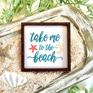 May include: A wooden sign with the text "take me to the beach" in teal blue lettering. The sign is decorated with a red starfish and a yellow sun.