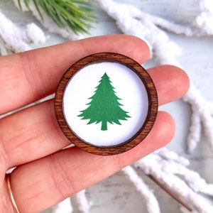 May include: A round wooden ornament with a white background and a green silhouette of a Christmas tree.
