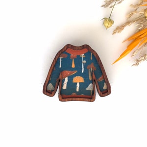 May include: A wooden sweater brooch with a blue and orange mushroom pattern.