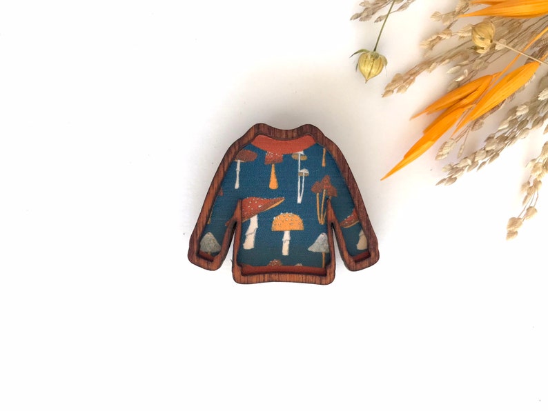 May include: A wooden sweater brooch with a blue and orange mushroom pattern.
