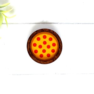 May include: A wooden coaster with a round, yellow pizza with red pepperoni slices on top.