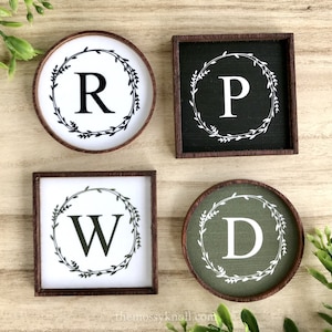 May include: Four wooden signs with a wreath and letter design. The signs are in different colors and feature the letters R, P, W, and D.