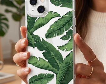 May include: Clear phone case featuring a vibrant pattern of green banana leaves on a white background. The case is held up by a person. The design is a tropical, botanical theme.