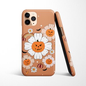 Pu&ograve; includere: Una custodia per telefono color beige con un tema di Halloween. La custodia presenta fiori bianchi con facce di zucca arancioni e un arcobaleno.