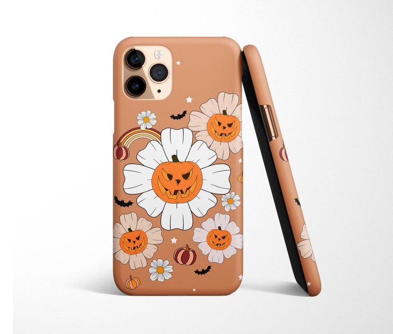 Pu&ograve; includere: Una custodia per telefono color beige con un tema di Halloween. La custodia presenta fiori bianchi con facce di zucca arancioni e un arcobaleno.
