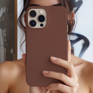 以下が含まれることがあります： マット仕上げの無地の茶色の携帯電話ケース。ケースは、角が丸く、カメラの切り欠きがある長方形です。携帯電話ケースは、スマートフォンを傷や損傷から保護するように設計されています。