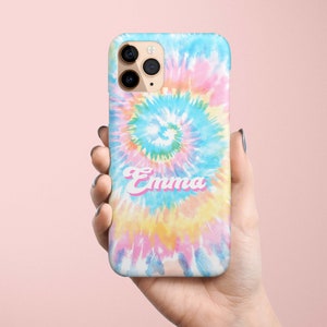 May include: A colorful phone case with a tie-dye design in shades of blue, pink, yellow, and green. The name "Emma" is written in a cursive font across the front of the case. The phone case is held in a hand.
