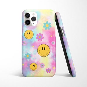 May include: A phone case with a tie-dye background featuring yellow smiley faces and colorful flowers. The case has a cutout for the camera lens.