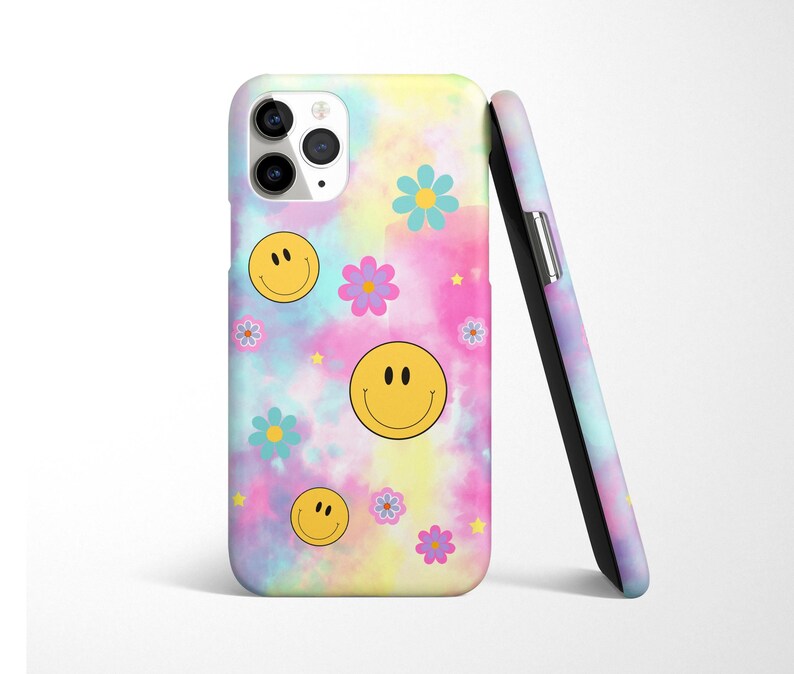 May include: A phone case with a tie-dye background featuring yellow smiley faces and colorful flowers. The case has a cutout for the camera lens.