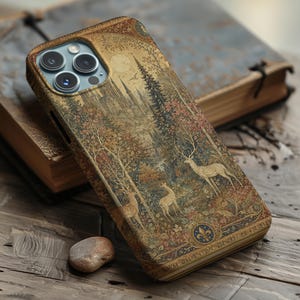May include: A smartphone case featuring a detailed tapestry-style print of a forest scene with deer, tall trees, and a distant castle under a moon. The design includes a gold-toned fleur-de-lis emblem at the bottom and a triple-lens camera cutout.