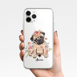 May include: A clear phone case with a white background and a colorful floral design featuring a pug wearing a flower crown. The text "Anna" is printed on the case.