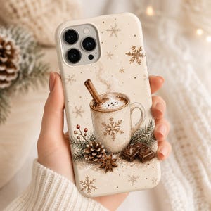 May include: A cream-colored phone case featuring a festive illustration of a steaming mug with a cinnamon stick, a pinecone, evergreen sprigs, star anise, and chocolate squares, all accented by gold-toned snowflakes and dots.