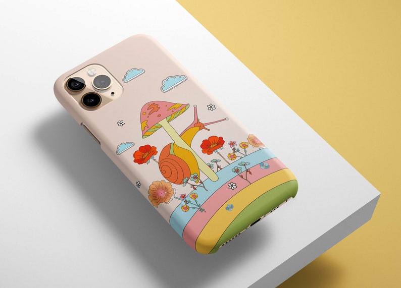 May include: A pink iPhone case with a colorful illustration of a snail on a mushroom with flowers and a rainbow.