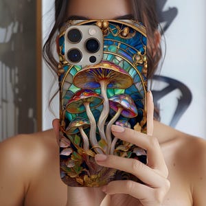May include: A colorful phone case featuring a stained-glass design with vibrant mushrooms. The case has a gold border and a blue background, with detailed artwork of the fungi in shades of red, purple, and orange. The case is held up in front of a person.