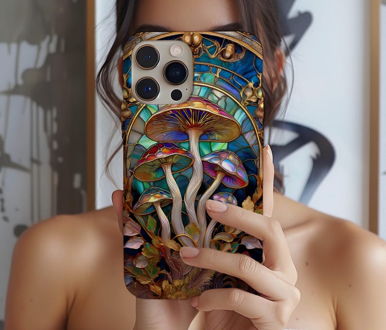 May include: A colorful phone case featuring a stained-glass design with vibrant mushrooms. The case has a gold border and a blue background, with detailed artwork of the fungi in shades of red, purple, and orange. The case is held up in front of a person.