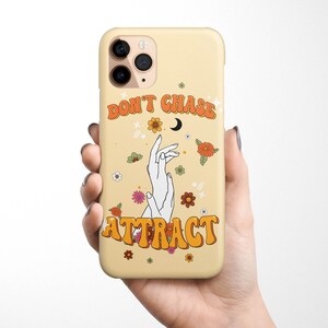 Może przedstawiać: Ż&oacute;łte etui na telefon z kwiatowym wzorem i napisem "Don't Chase Attract" w pomarańczowych literach. Etui ma wycięcie na obiektyw aparatu.