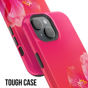 May include: A pink phone case with a floral design. The case has a raised camera bump and a cutout for the phone's buttons. The case is made of a durable material and is designed to protect your phone from scratches and drops.  TOUGH CASE