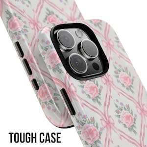 May include: A white phone case with a pink and white floral pattern and pink bows. The case has a cutout for the camera lens. The text "TOUGH CASE" is printed on the bottom of the image.