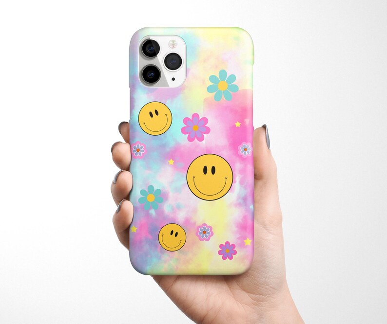 May include: A phone case with a tie-dye background and yellow smiley faces and pink, blue, and purple flowers.