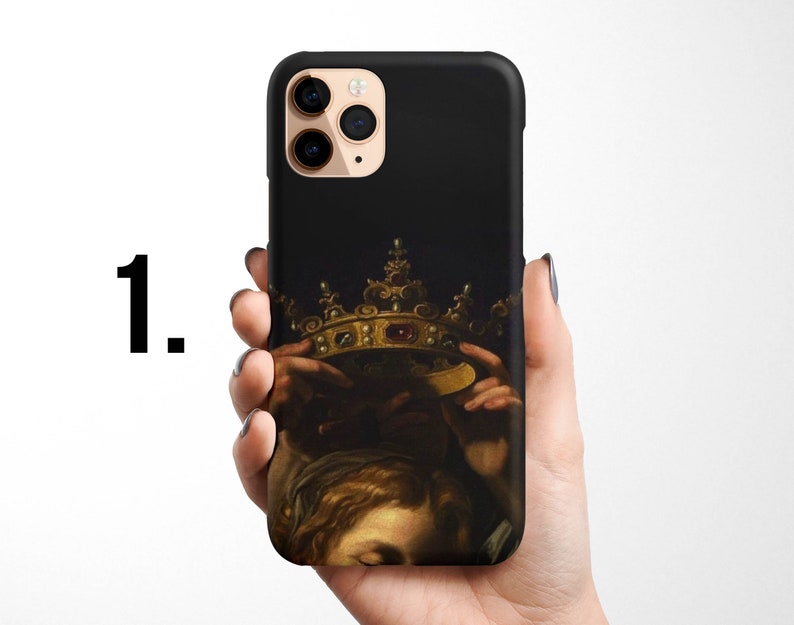 Pode incluir: Uma capa preta para iPhone com uma coroa dourada e uma pintura de uma pessoa usando a coroa. A capa tem um recorte para a lente da c&acirc;mera.