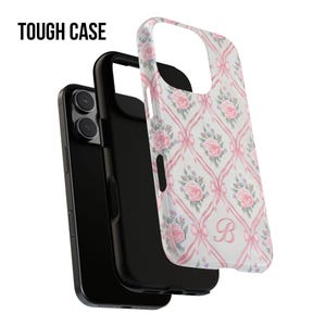 May include: A tough case for a phone with a pink floral pattern and a white letter "B" in the center. The case is made of durable plastic and has a raised lip to protect the screen.