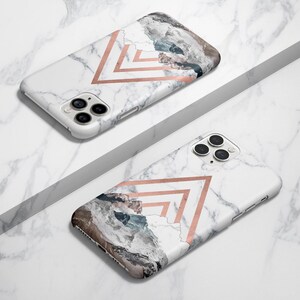 K&ouml;nnte beinhalten: Zwei wei&szlig;e iPhone-H&uuml;llen mit Marmormuster und geometrischen Designs in Ros&eacute;gold. Eine H&uuml;lle hat ein Bergketten-Design und die andere ein schlichtes geometrisches Design.