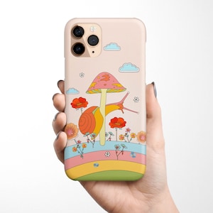 May include: A pink and white iPhone case with a cartoon snail and mushroom design. The snail is crawling on a mushroom with a pink and white cap. The background is a rainbow with flowers and clouds.