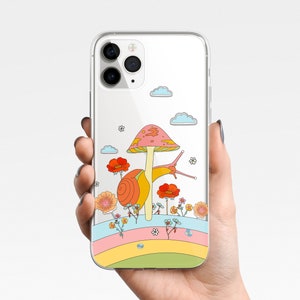 May include: Clear phone case featuring a colorful illustration of a snail, mushroom, flowers, and clouds. The design includes a rainbow-colored stripe at the bottom. The case is held in a person's hand.