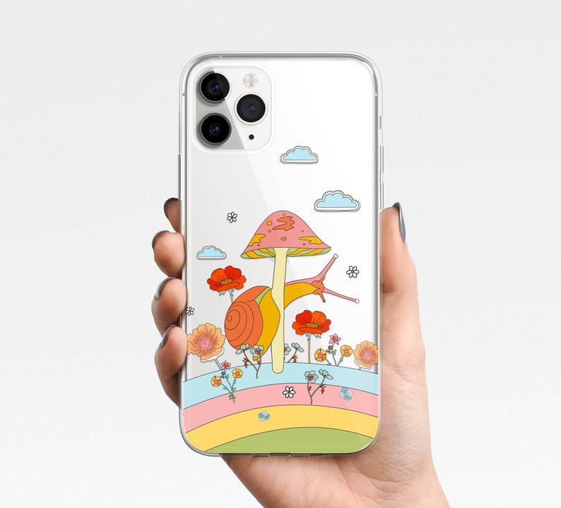 May include: Clear phone case featuring a colorful illustration of a snail, mushroom, flowers, and clouds. The design includes a rainbow-colored stripe at the bottom. The case is held in a person's hand.