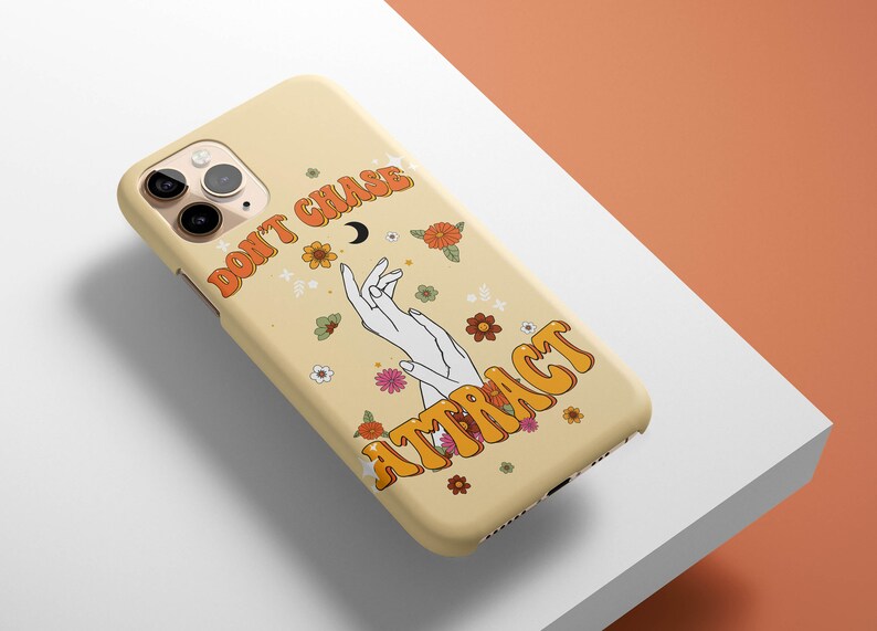 Może przedstawiać: Ż&oacute;łte etui na iPhone'a z kwiatowym wzorem i tekstem "Don't Chase, Attract" w retro czcionce.